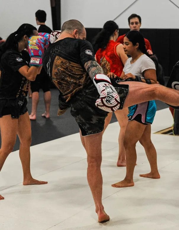 Group of athletes practicing muay thai kicks on pads during partner drills at Muaythai Iayrin